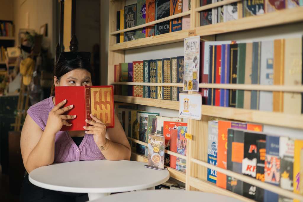 Woman mischievously smiling behind a book while looking at a signage